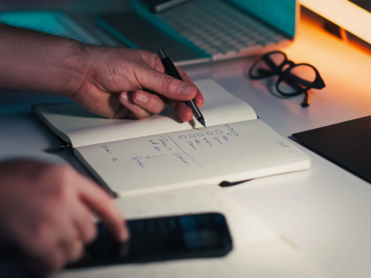 A person documenting a structured task list beside a laptop